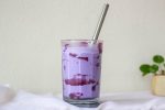 Tall clear glass filled with bright purple ube milkshake