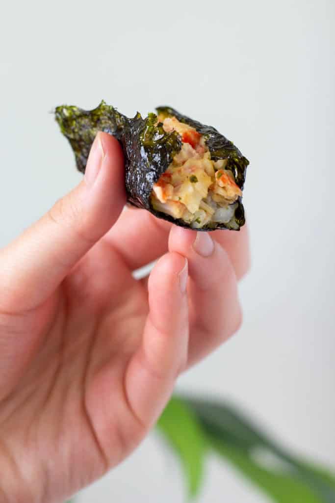 Hand holding little bundle of seaweed wrapped around rice and baked imitation crab salad.