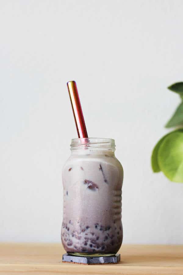 Small glass jar full of ombre maroon liquid, with the light colored milk tea at the top and maroon-colored sweet red bean at the bottom.